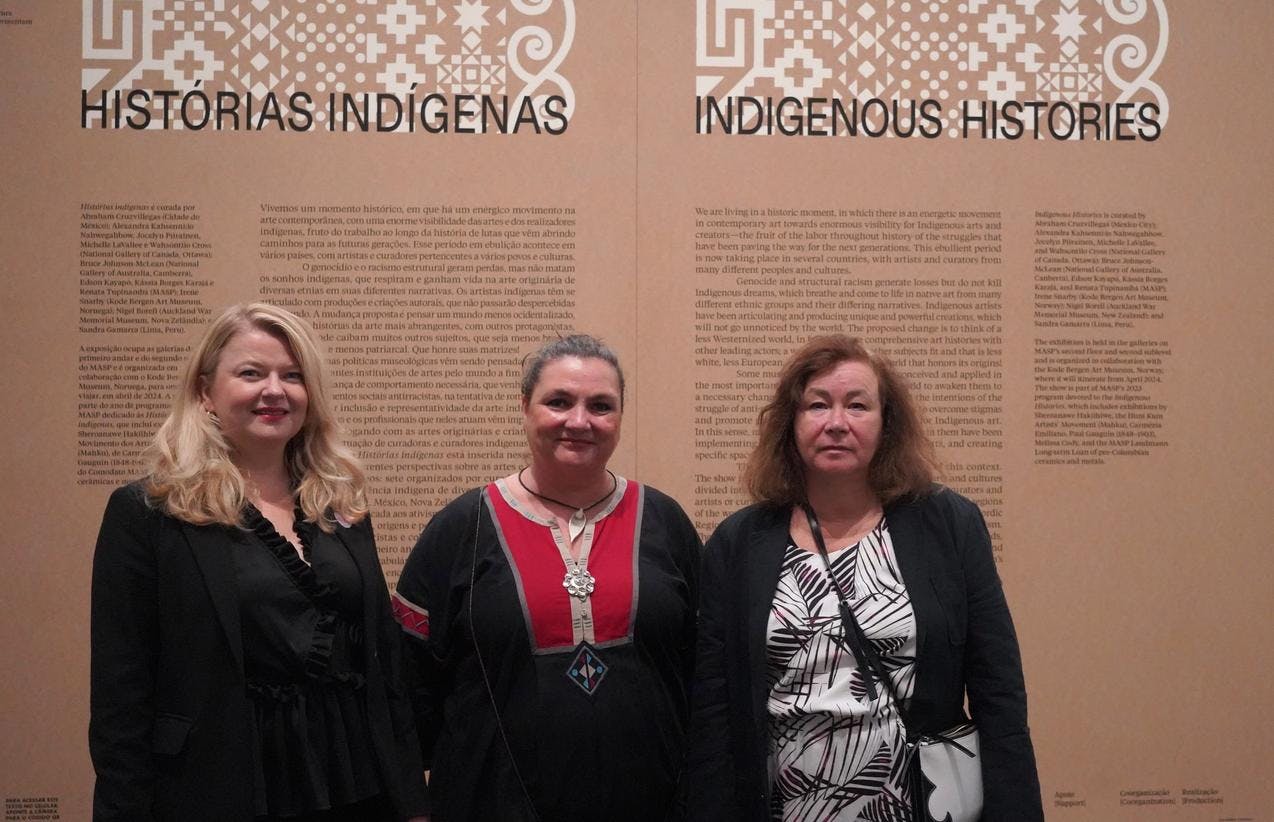 Tre kvinner står samlet foran en utstillingsvegg med tekst