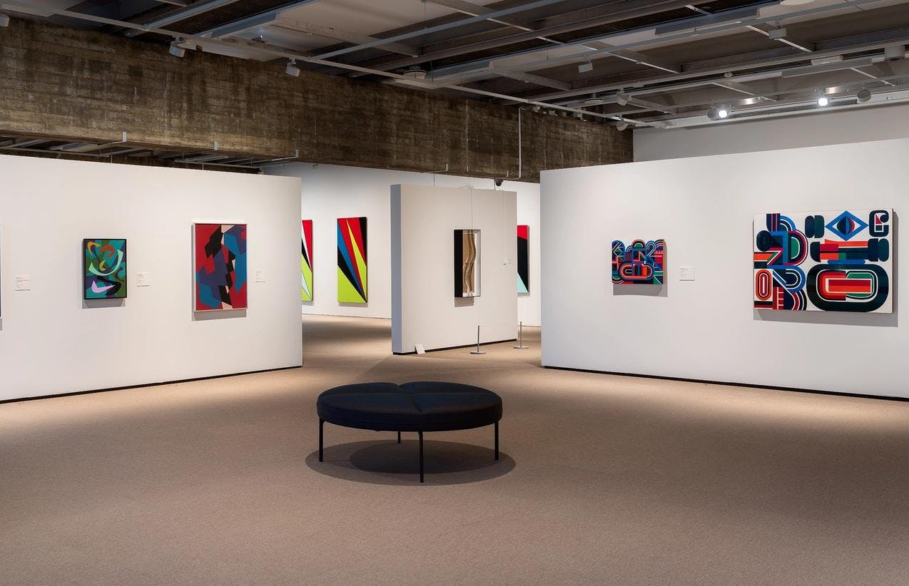An exhibition room with white walls, displaying colorful abstract paintings