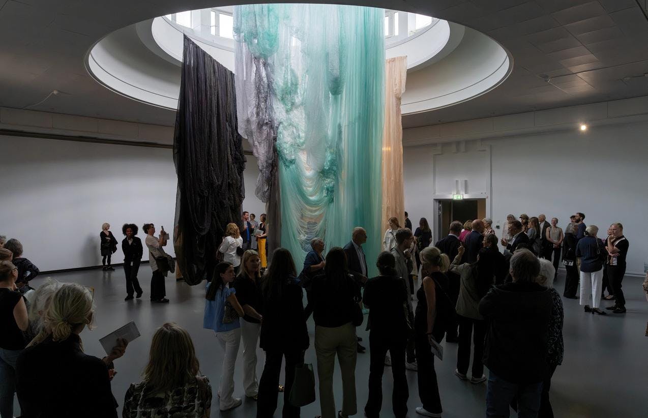 Overview of textile installation hanging from ceiling and a group of people in front.